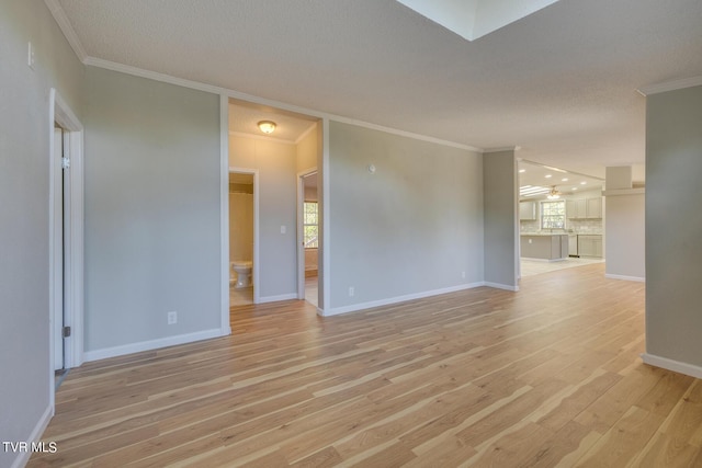 unfurnished room featuring light wood-style floors, baseboards, ornamental molding, and a textured ceiling