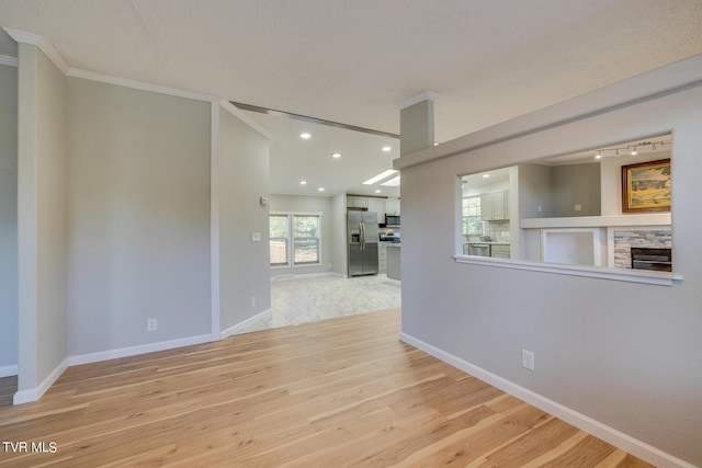 empty room featuring crown molding, baseboards, a stone fireplace, and wood finished floors