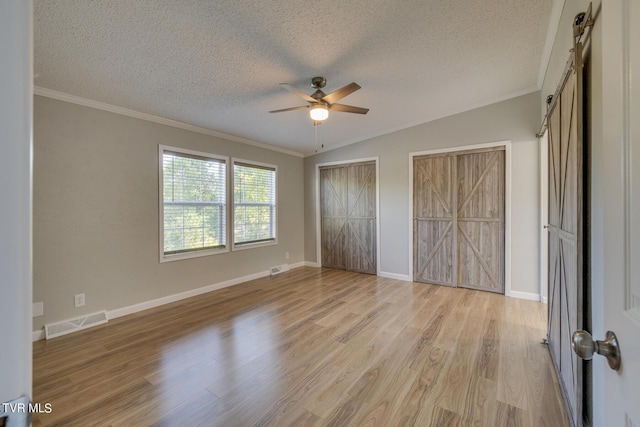 unfurnished bedroom with a textured ceiling, visible vents, a barn door, and ornamental molding