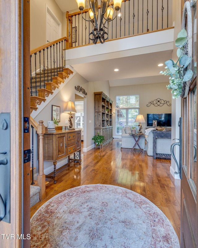 entrance foyer with a chandelier, hardwood / wood-style floors, stairs, baseboards, and a towering ceiling