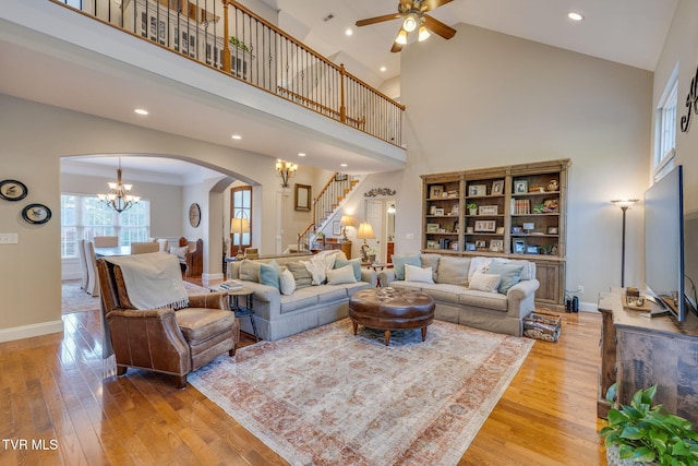 living area with arched walkways, stairway, high vaulted ceiling, ceiling fan with notable chandelier, and light wood-style flooring