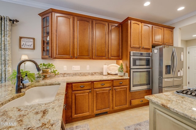 kitchen featuring ornamental molding, light stone countertops, glass insert cabinets, a sink, and stainless steel appliances
