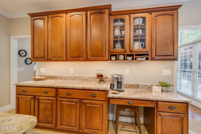 kitchen with crown molding, decorative backsplash, light stone countertops, glass insert cabinets, and baseboards