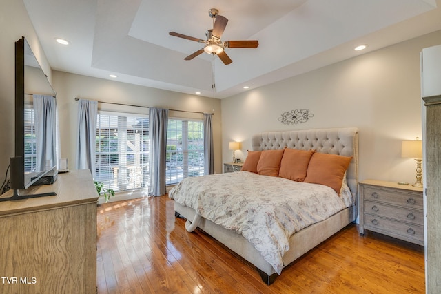 bedroom featuring recessed lighting, a ceiling fan, a tray ceiling, and light wood-type flooring