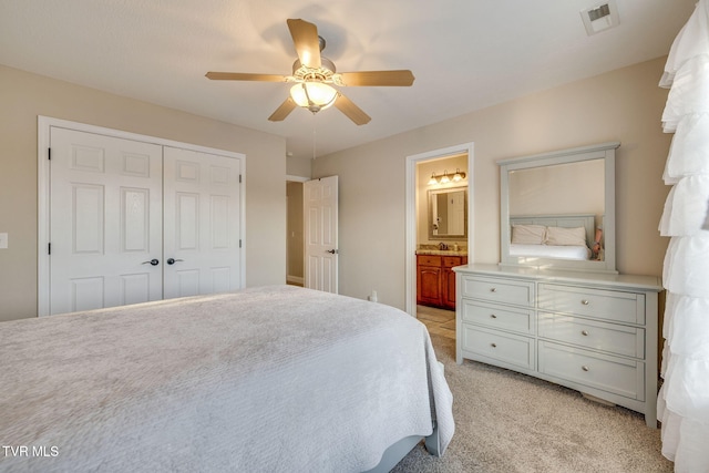 bedroom with visible vents, a closet, ensuite bathroom, light colored carpet, and a ceiling fan