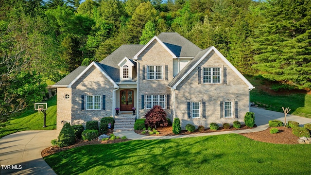 view of front of home featuring brick siding, a front yard, and a forest view