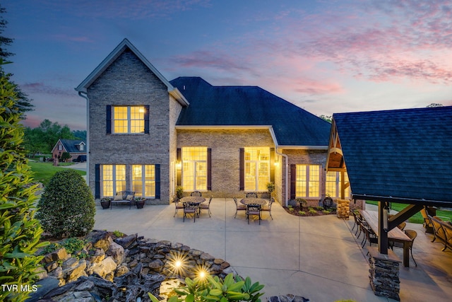 back of house at dusk featuring brick siding and a patio area