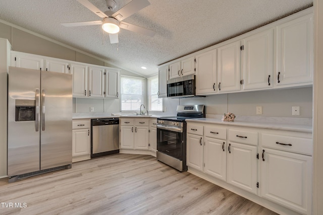 kitchen featuring a textured ceiling, vaulted ceiling, a sink, white cabinets, and stainless steel appliances