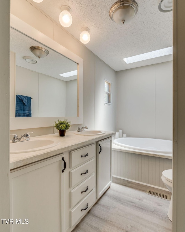 bathroom featuring a sink, a skylight, double vanity, and wood finished floors