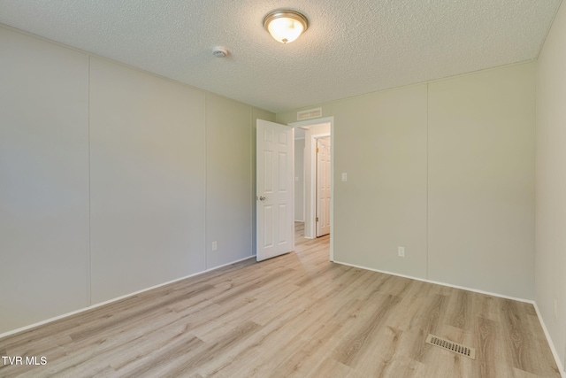 empty room featuring visible vents, a textured ceiling, and wood finished floors