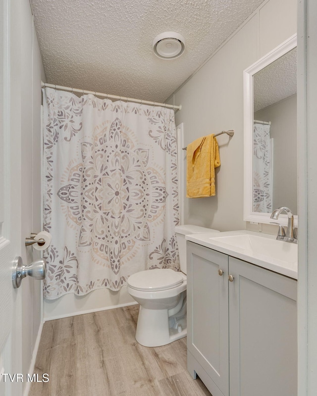 bathroom with a textured ceiling, wood finished floors, shower / tub combo, vanity, and toilet