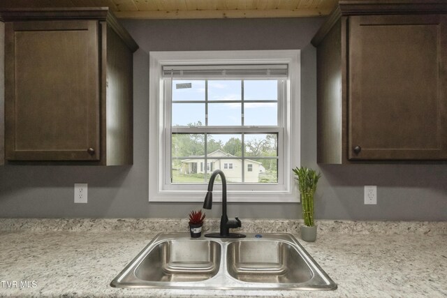 kitchen featuring light countertops, dark brown cabinets, wooden ceiling, and a sink