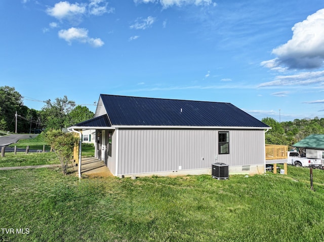 view of side of property with a lawn, central AC unit, metal roof, and crawl space