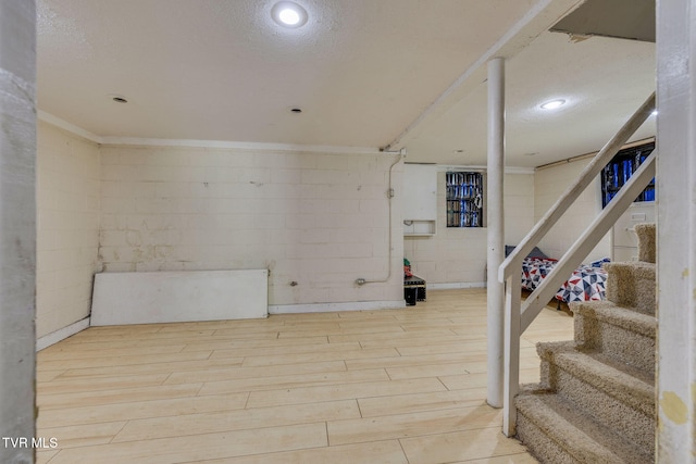 finished basement featuring stairway, concrete block wall, and wood finished floors