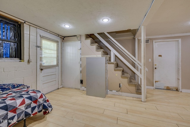 below grade area featuring stairs, a textured ceiling, visible vents, and wood finished floors