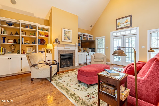 living area featuring a tiled fireplace, high vaulted ceiling, french doors, and light wood-type flooring