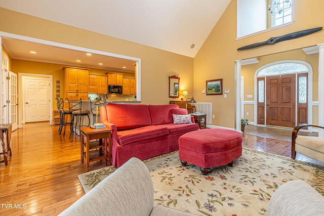 living room featuring recessed lighting, high vaulted ceiling, light wood-type flooring, and ornate columns