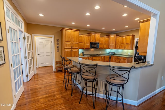 kitchen featuring brown cabinetry, backsplash, crown molding, black appliances, and a breakfast bar