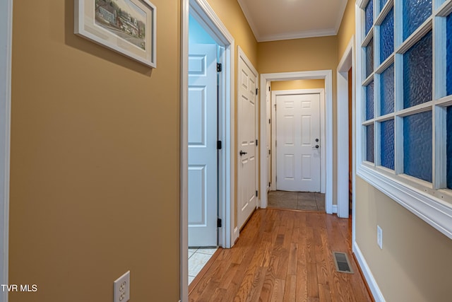 hallway featuring baseboards, ornamental molding, light wood-style flooring, and visible vents