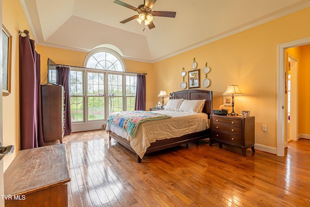 bedroom featuring wood-type flooring, crown molding, baseboards, ceiling fan, and a raised ceiling
