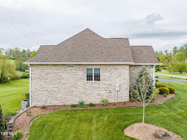 view of side of property with a yard, brick siding, and roof with shingles