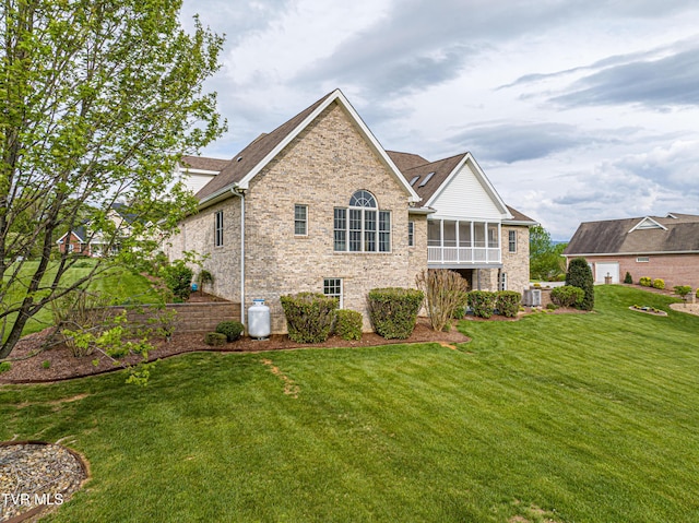 back of property featuring central air condition unit, stone siding, brick siding, a sunroom, and a lawn