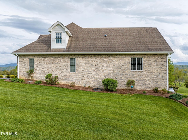 view of side of home featuring a yard, brick siding, and a shingled roof