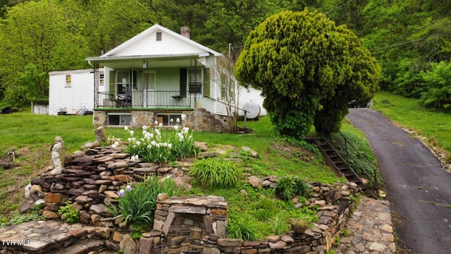 view of front of house with covered porch, a view of trees, a front lawn, and stairs