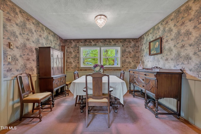 dining room featuring a textured ceiling, a wainscoted wall, and wallpapered walls