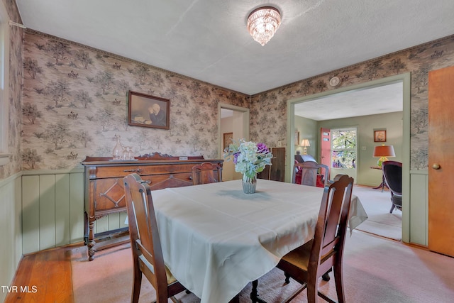 carpeted dining space with a wainscoted wall and wallpapered walls