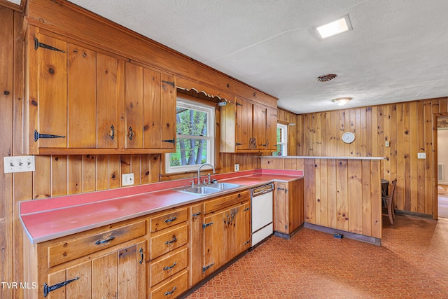 kitchen featuring brown cabinets, white dishwasher, a sink, a textured ceiling, and a peninsula