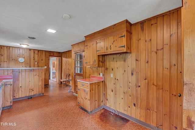kitchen featuring wood walls, baseboards, light countertops, tile patterned floors, and brown cabinets