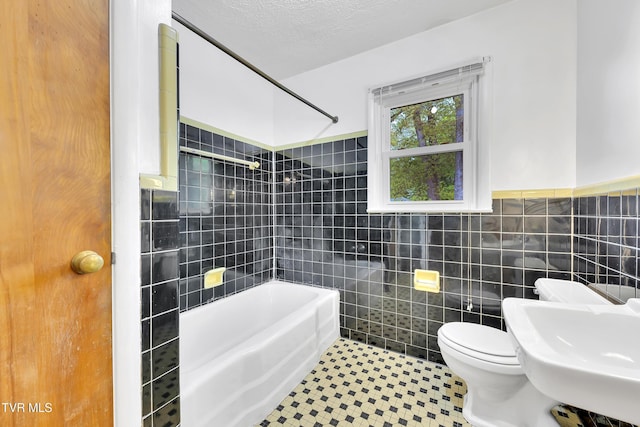 bathroom with a sink, tile walls, shower / bathing tub combination, and toilet