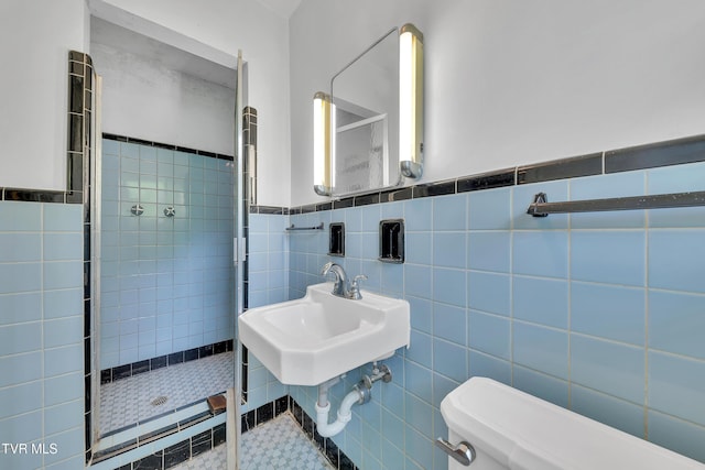 bathroom with tile walls, wainscoting, a stall shower, a sink, and toilet