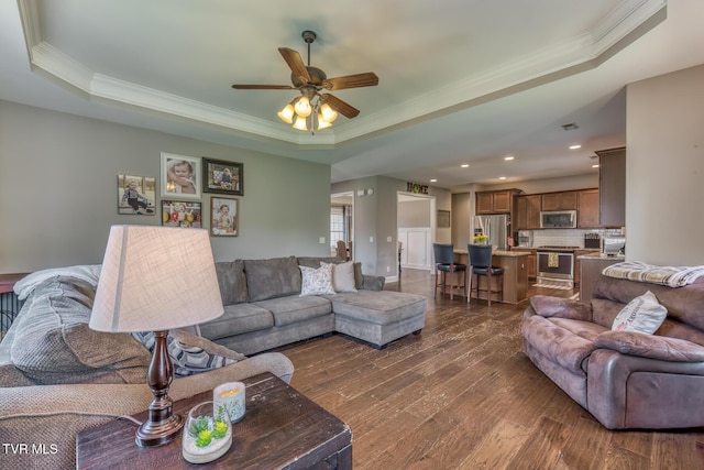living room with ornamental molding, a raised ceiling, a ceiling fan, and dark wood finished floors