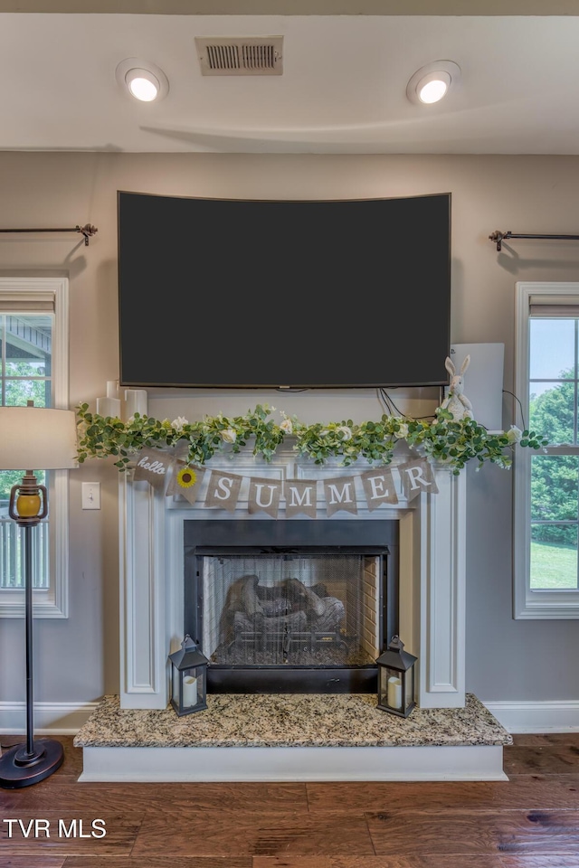 details featuring a fireplace with raised hearth, baseboards, visible vents, and wood finished floors