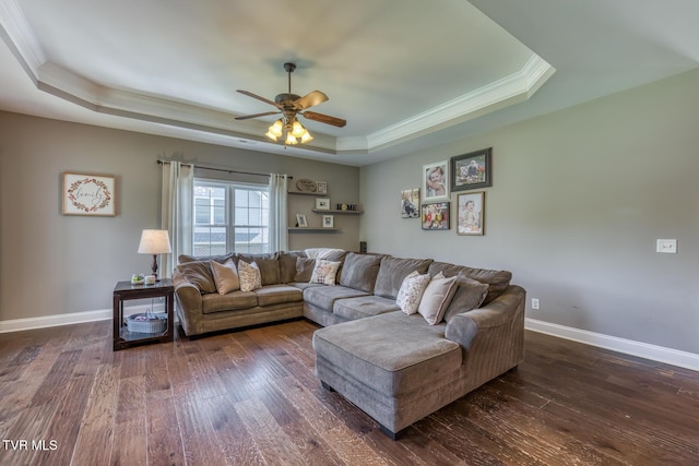 living area with crown molding, ceiling fan, a raised ceiling, baseboards, and dark wood-type flooring