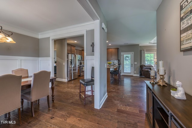 dining area featuring a notable chandelier, a decorative wall, dark wood finished floors, a wainscoted wall, and ornamental molding