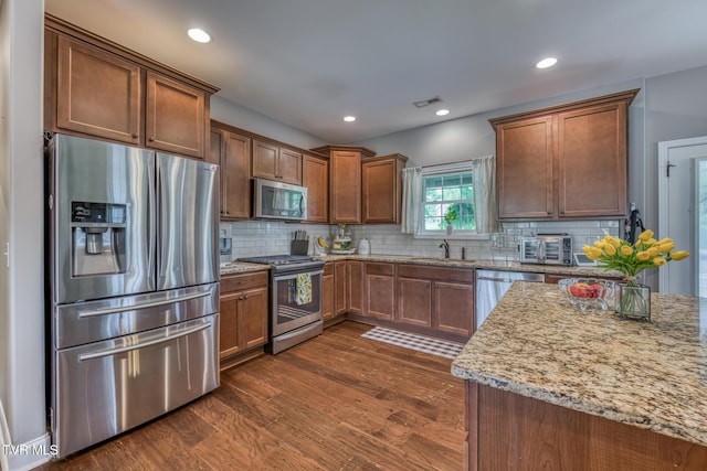 kitchen featuring appliances with stainless steel finishes, light stone counters, a sink, recessed lighting, and backsplash