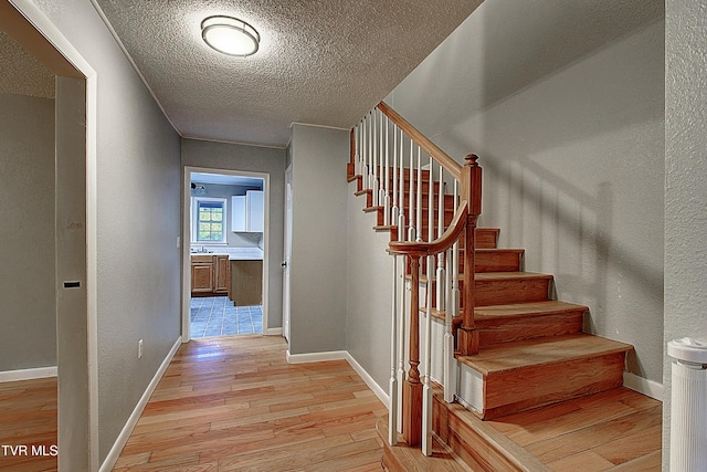 staircase featuring a textured ceiling, baseboards, a textured wall, and wood finished floors