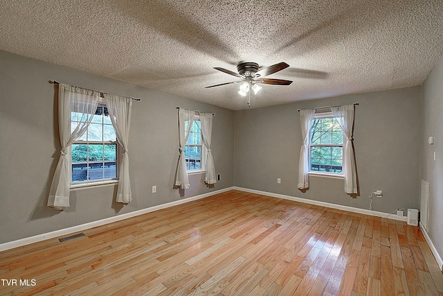 empty room featuring a wealth of natural light, light wood-style flooring, ceiling fan, and visible vents