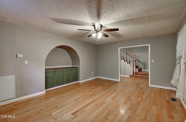 unfurnished room featuring ceiling fan, a textured ceiling, stairs, light wood-type flooring, and visible vents