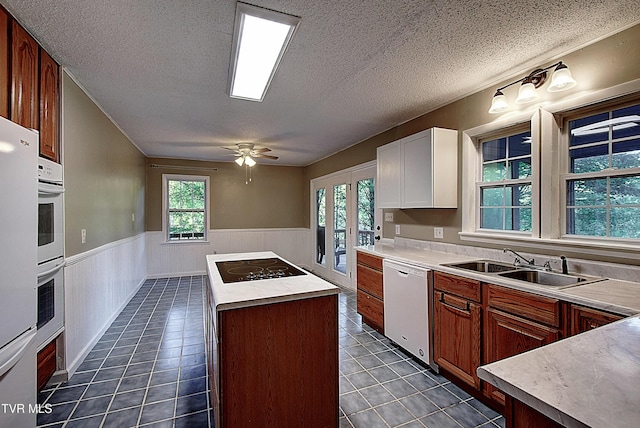 kitchen with white dishwasher, a center island, a sink, a wainscoted wall, and black electric stovetop