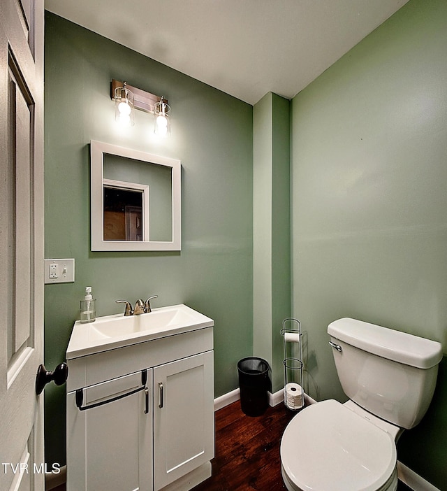 half bath featuring vanity, baseboards, wood finished floors, and toilet