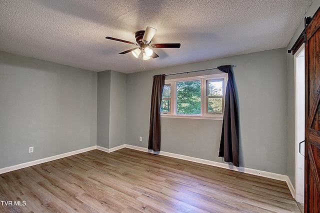 unfurnished room with a ceiling fan, a textured ceiling, a barn door, wood finished floors, and baseboards