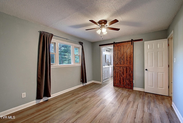 unfurnished bedroom with baseboards, a barn door, a textured ceiling, and wood finished floors