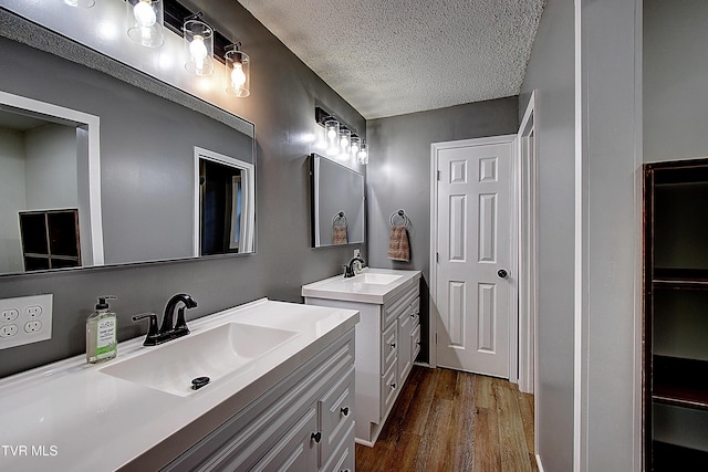 full bathroom featuring a sink, a textured ceiling, wood finished floors, and two vanities