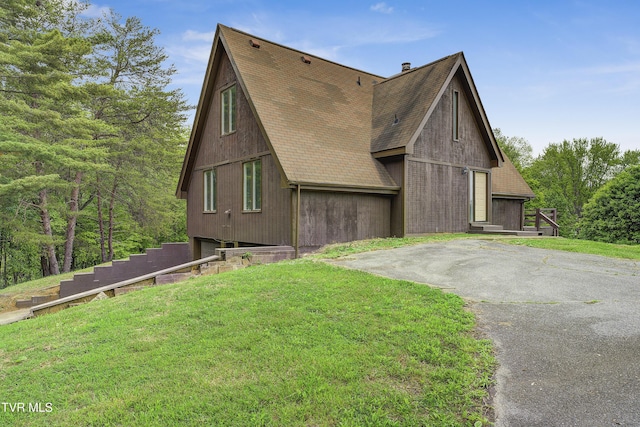 view of front of house with a front yard, roof with shingles, and driveway