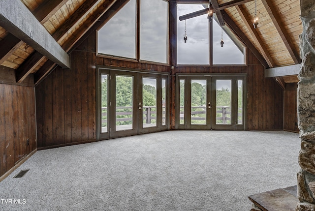 unfurnished living room featuring wooden ceiling, beamed ceiling, wood walls, healthy amount of natural light, and french doors