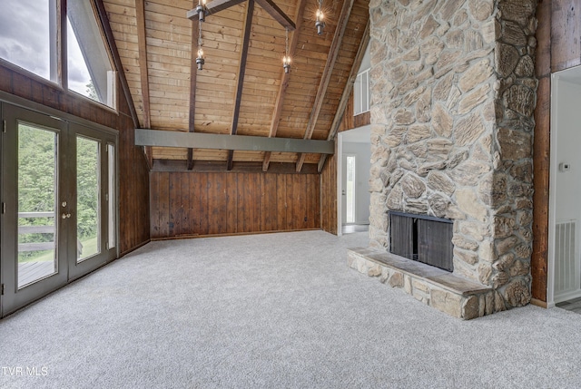 unfurnished living room featuring wood ceiling, carpet flooring, wooden walls, beamed ceiling, and a stone fireplace